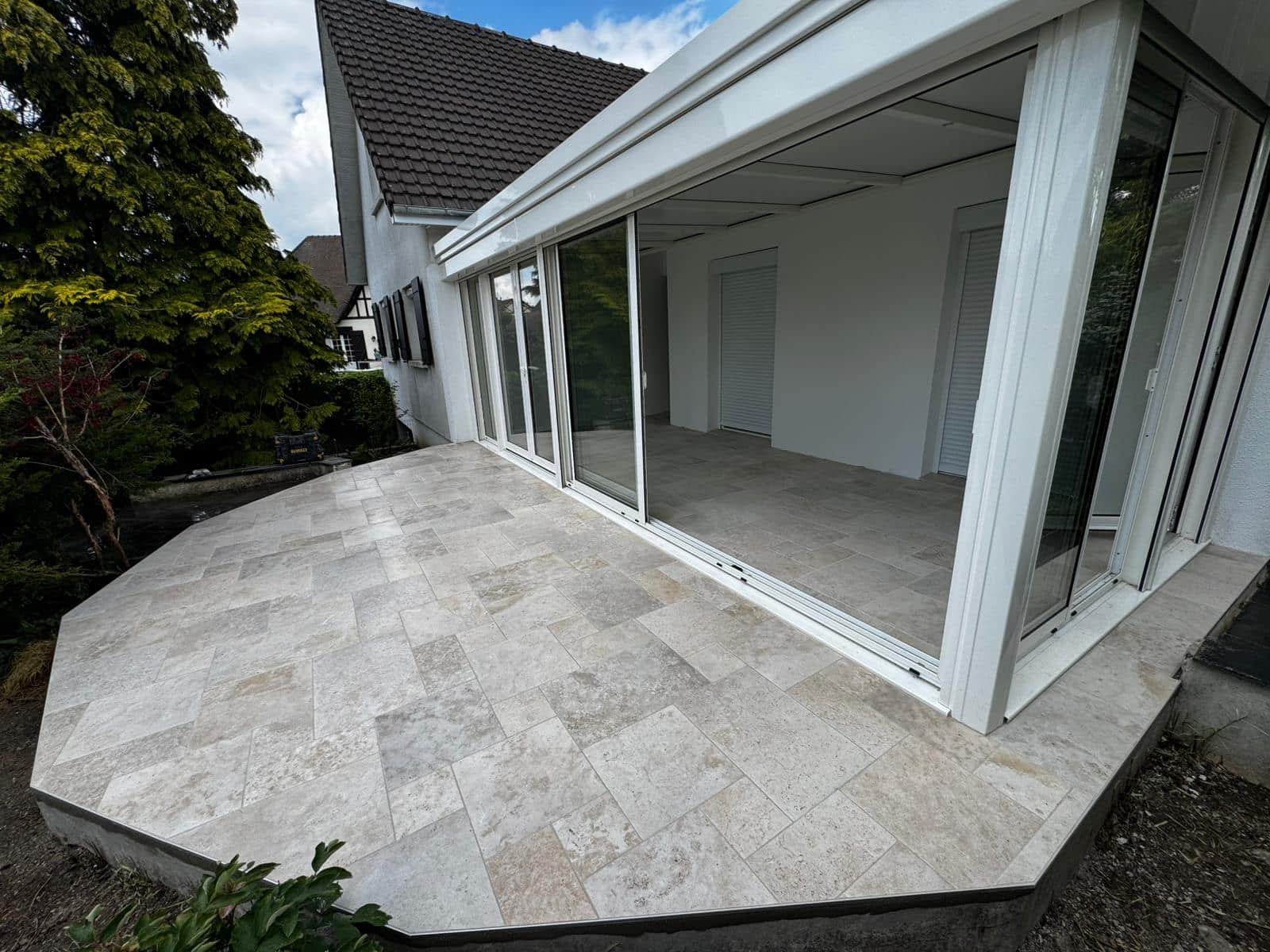 Terrasse en travertin beige posée devant une véranda vitrée, rénovation extérieure MVT Réno
