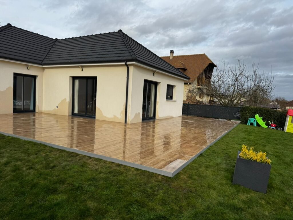 Terrasse en carrelage effet bois devant une maison beige avec pelouse, réalisation MVT RENO